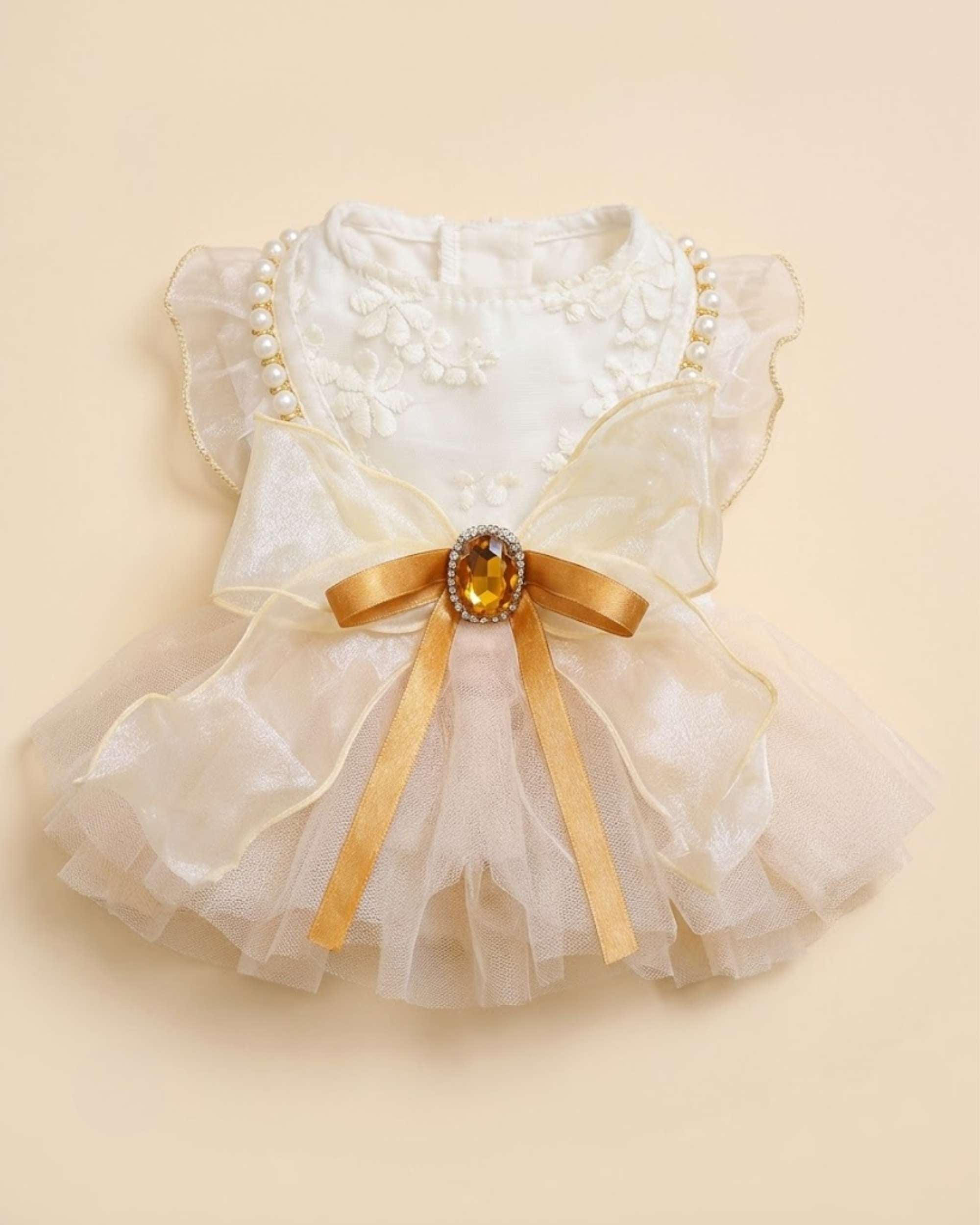Top-down flat lay photograph of the champagne gold pet dress featuring the large organza bow, amber jewel, and pearl-trimmed flutter sleeves.