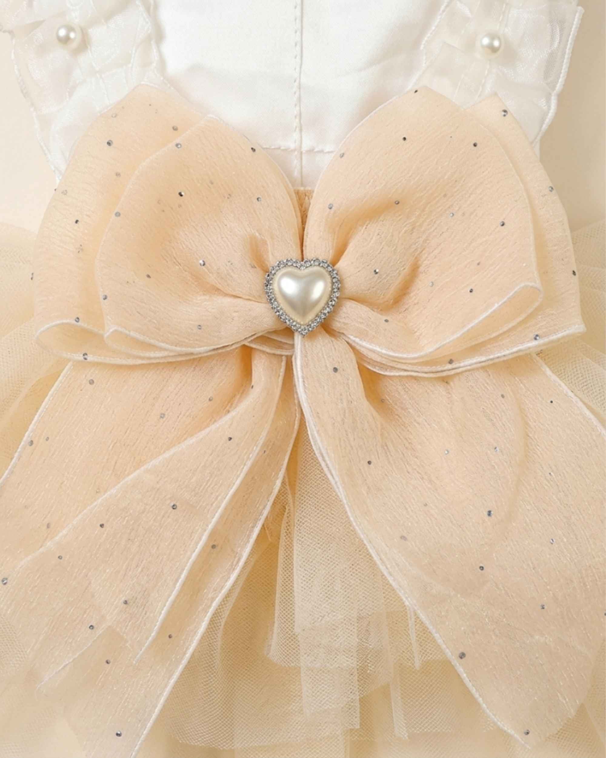 Close-up of the champagne bow with scattered sparkle accents and a faux-pearl heart ornament
