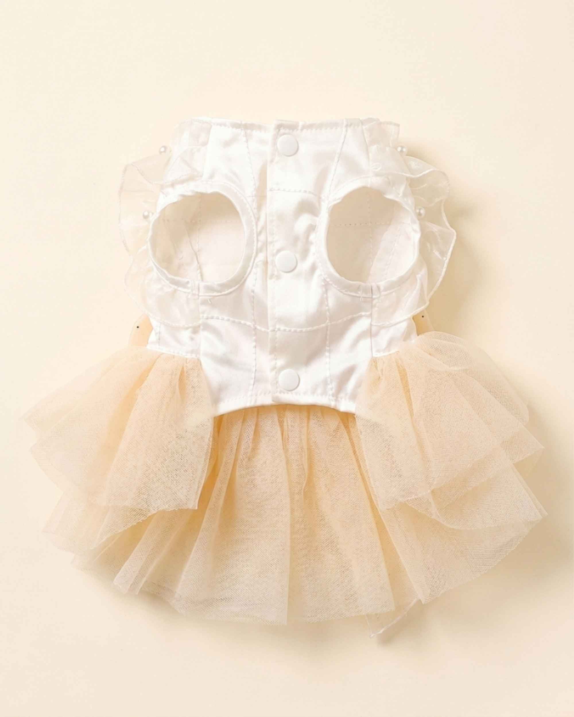 Front flat lay of the pet dress showing its white satin bodice, arm openings, ruffles, snap buttons and champagne tulle skirt