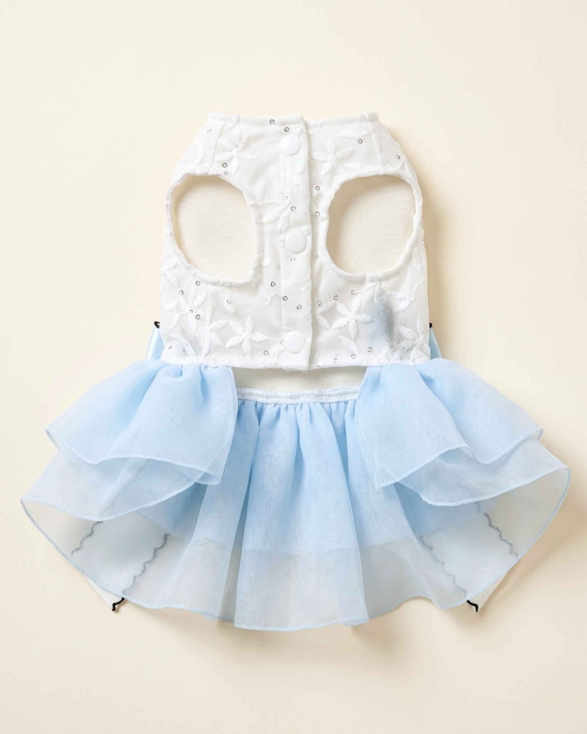 Closure-side flat lay showing the white embroidered bodice, three covered snap fasteners, arm openings and blue skirt attachment