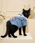 Black cat wearing the Denim Blue Double-Breasted Pet Tuxedo in an elegant celebration setting with soft ivory flowers.