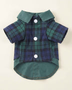 Closure-side flat lay of the green and navy plaid pet shirt showing three white snap buttons, short sleeves, contrasting collar and rounded shirt hem.