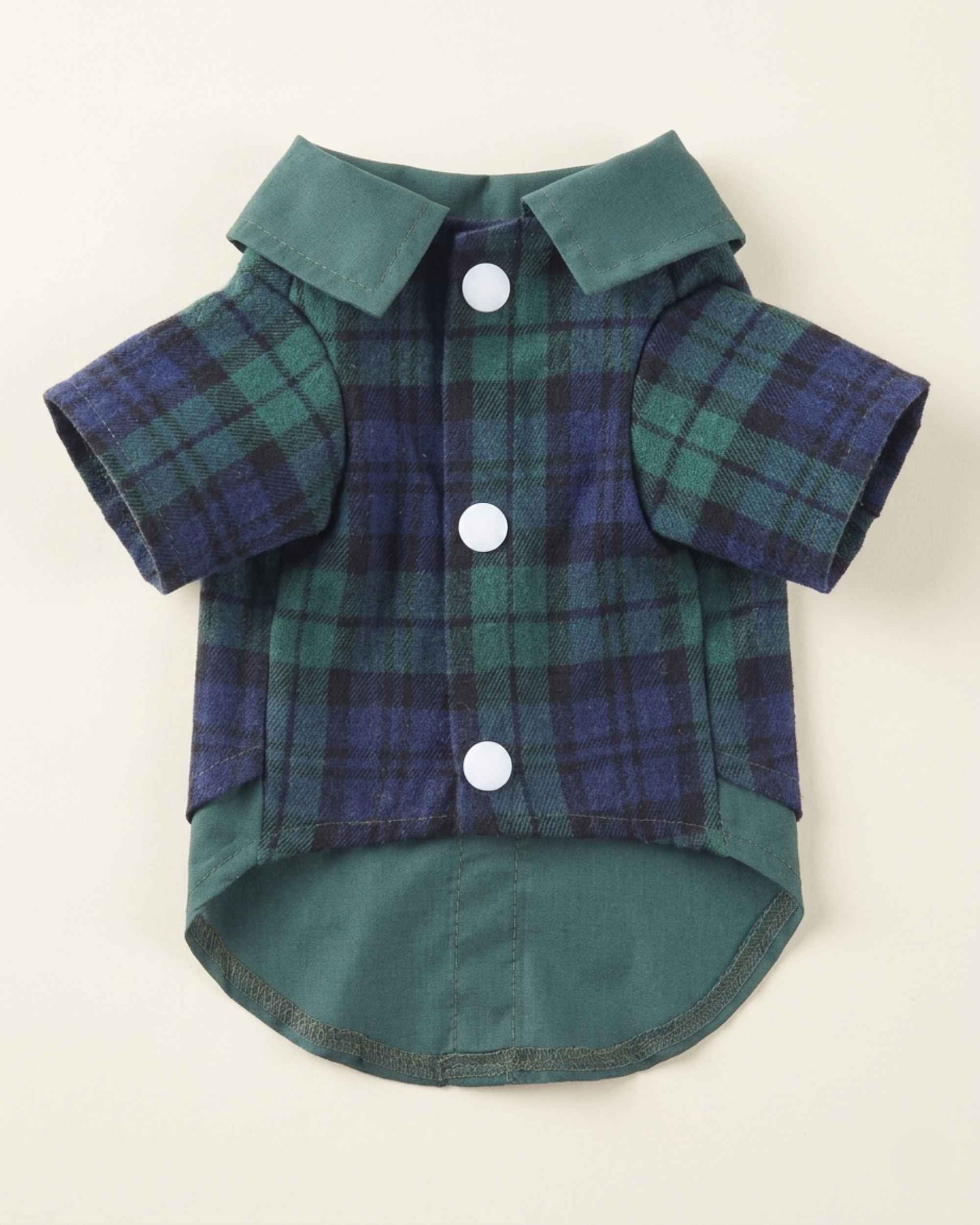Closure-side flat lay of the green and navy plaid pet shirt showing three white snap buttons, short sleeves, contrasting collar and rounded shirt hem.