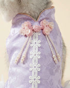 Close-up of pink floral knot ornaments, hanging pearl tassels and white lace trim on a lavender jacquard pet dress.