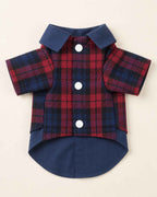 Closure-side flat lay of the navy and red plaid pet shirt showing three white snap buttons, navy collar, short sleeves and rounded navy shirt hem.