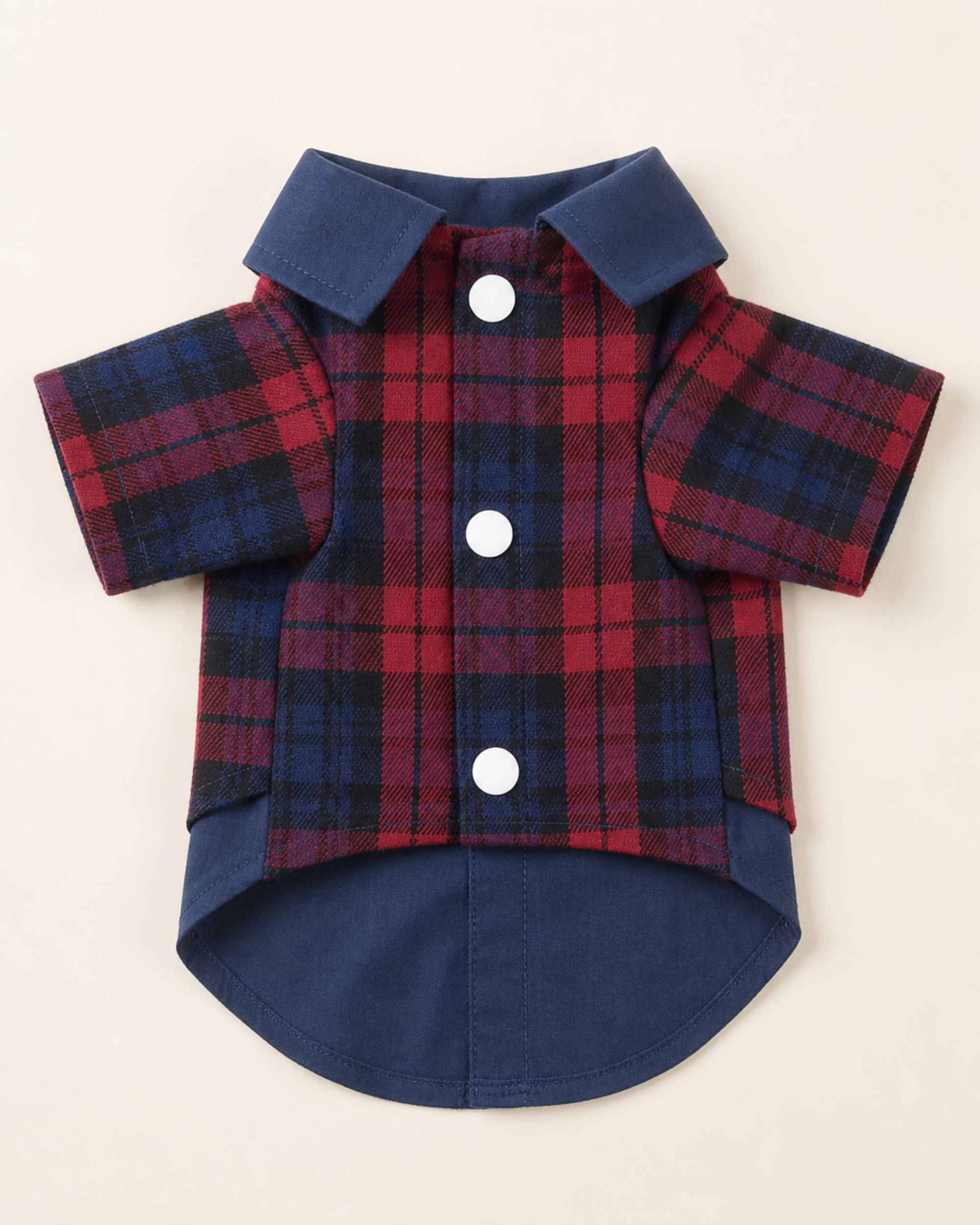 Closure-side flat lay of the navy and red plaid pet shirt showing three white snap buttons, navy collar, short sleeves and rounded navy shirt hem.