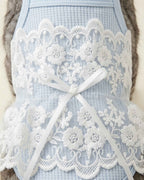 Close-up macro view of delicate white floral embroidery lace and white satin bow on soft blue waffle-knit fabric.