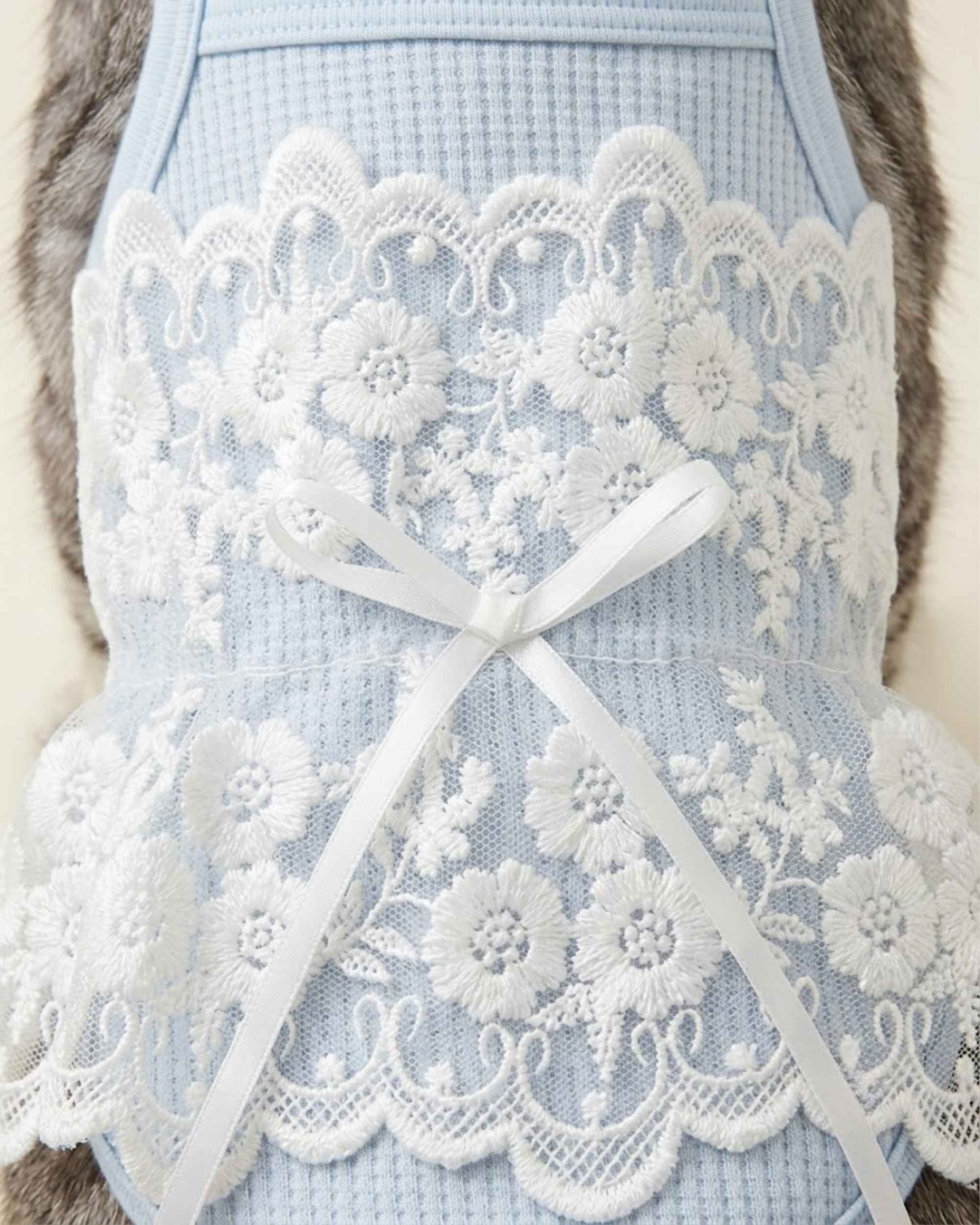 Close-up macro view of delicate white floral embroidery lace and white satin bow on soft blue waffle-knit fabric.