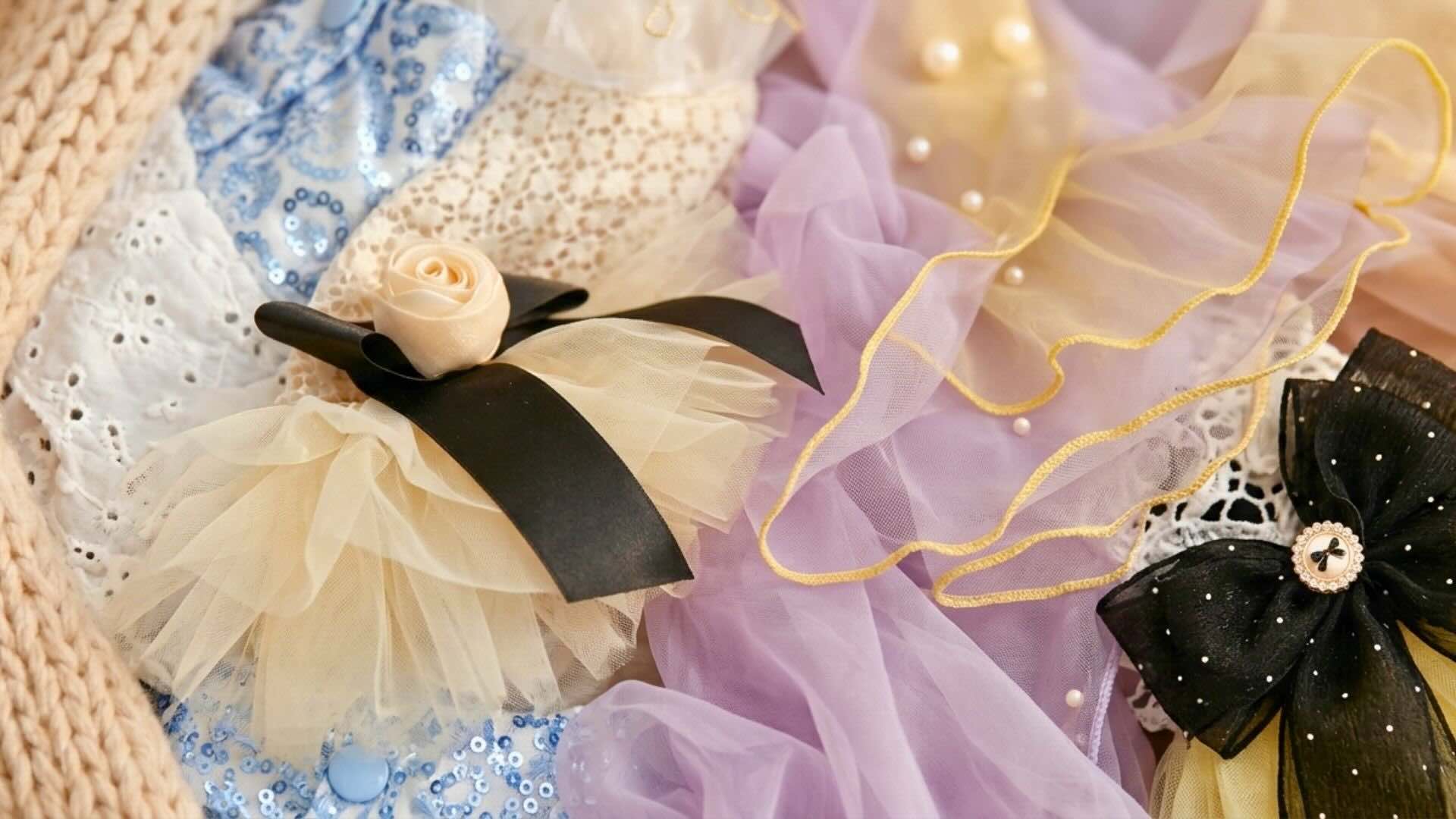 A premium Pet2Cute material collage with a cream knitted border, cream and light blue embroidered lace, ivory and lavender tulle ruffles, faux pearls, and a black and gold trim bow.