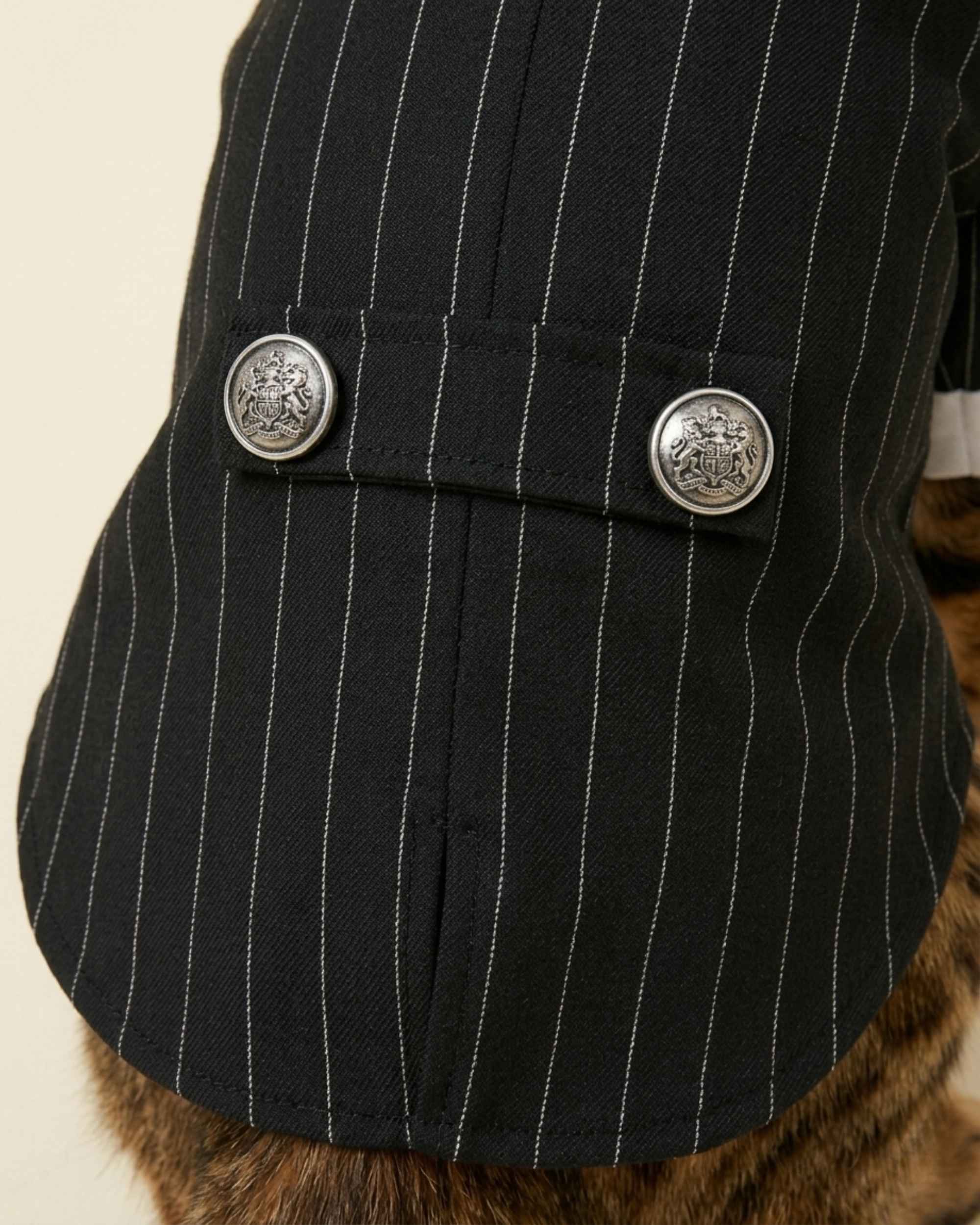 Close-up of the black pinstripe fabric, centre back seam and two embossed silver-tone buttons on the decorative rear tab