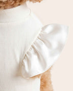 Close-up of the pearl-white satin shoulder ruffle, gathered seam and fine ivory micro-rib fabric on the pet turtleneck.