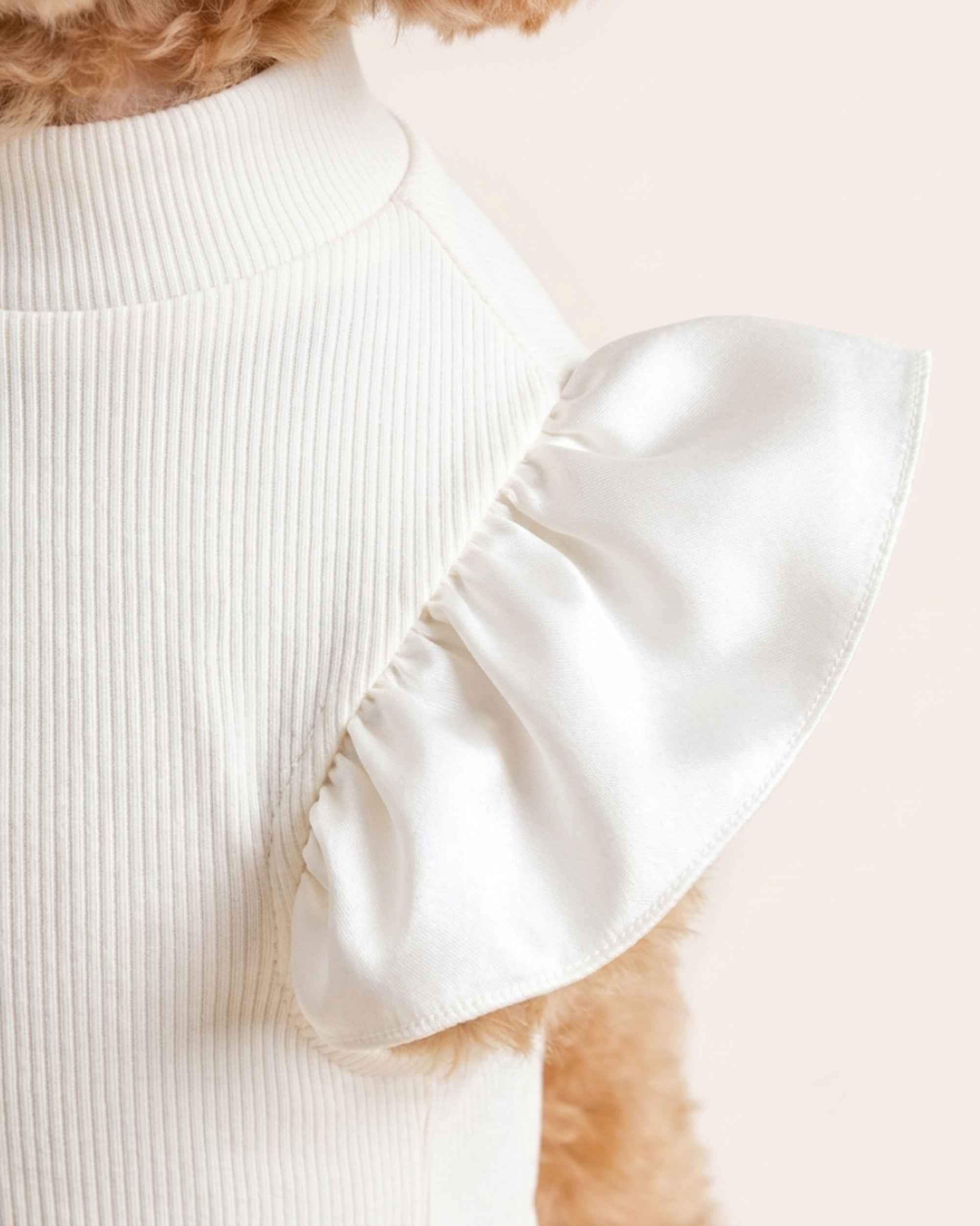 Close-up of the pearl-white satin shoulder ruffle, gathered seam and fine ivory micro-rib fabric on the pet turtleneck.