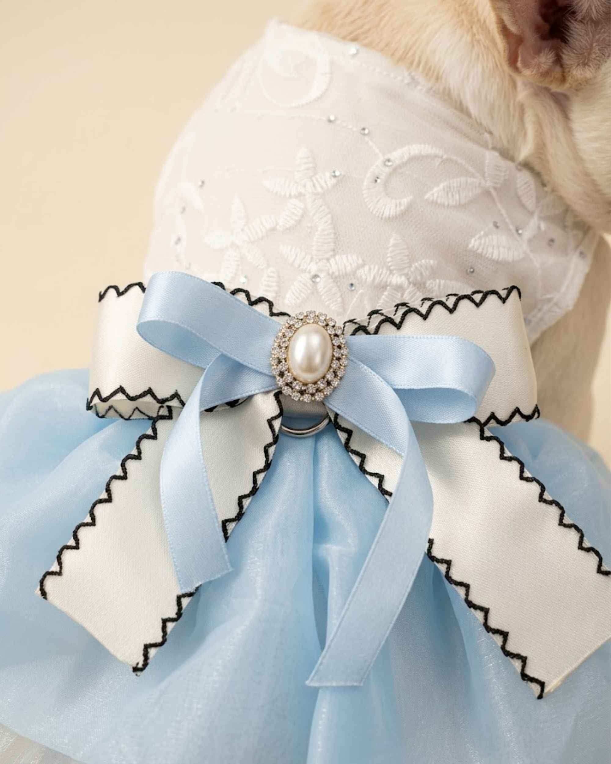 Close-up of the sky blue and ivory layered bow with black edge stitching and a pearl-style centre brooch.